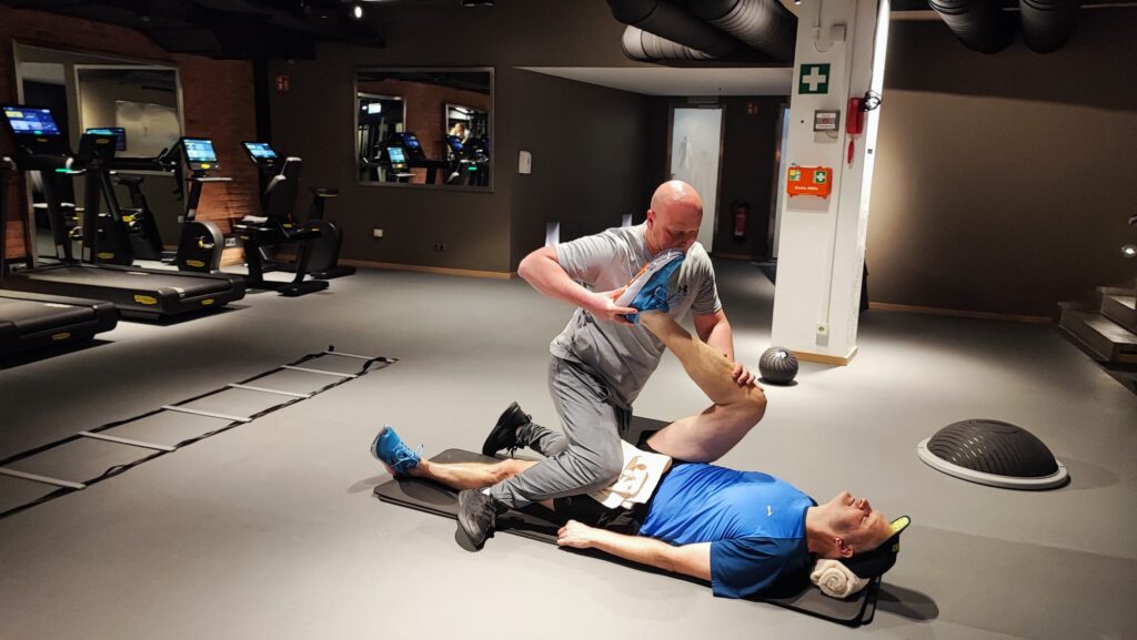 Ein Personal Trainer dehnt die Beinmuskulatur eines Kunden beim Assisted Stretching in einem Hamburger Fitnessstudio zur Steigerung der Flexibilität.